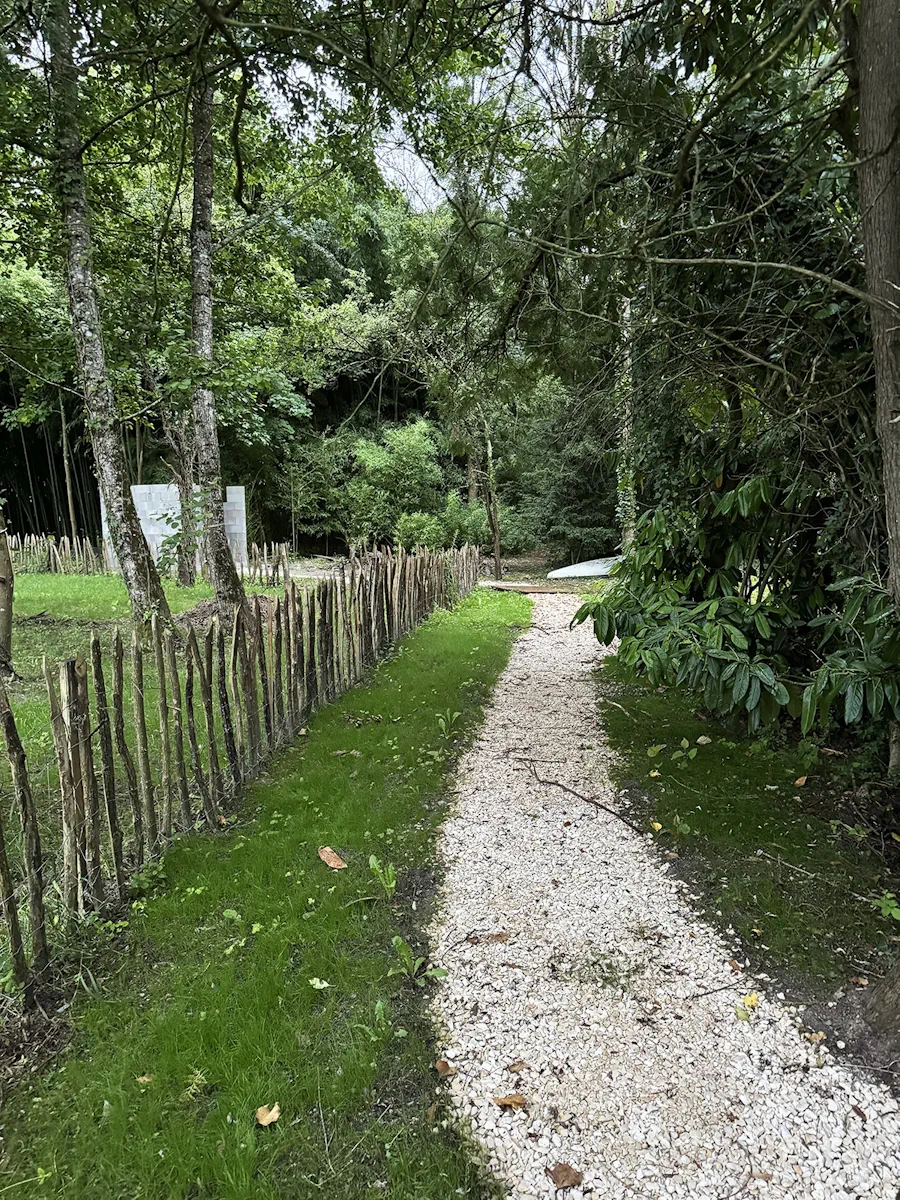Chemin en gravier blanc bordé d'une ganivelle en châtaignier, dans un jardin arboré
