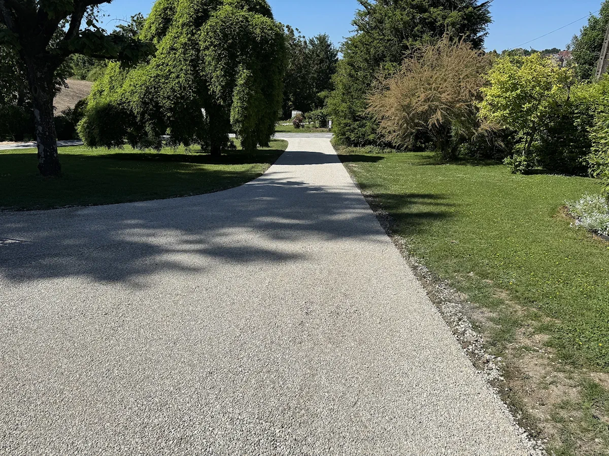 Allée en gravier stabilisé traversant un parc arboré, tracé en pente douce