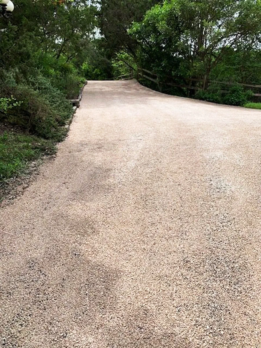 Allée en gravier stabilisé décrivant une longue courbe sous les arbres, bordée d'une barrière en bois