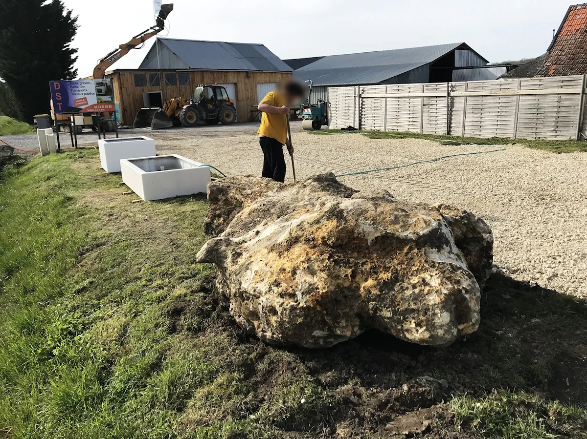 Compagnon ajustant la terre autour d'un gros bloc de pierre posé en bordure de cour