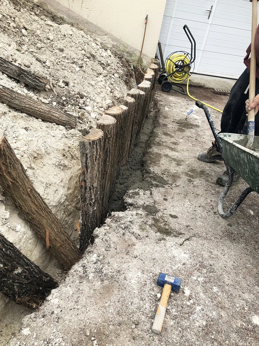 Bordure en rondins de bois alignés dans une tranchée, hauteurs ajustées au terrain