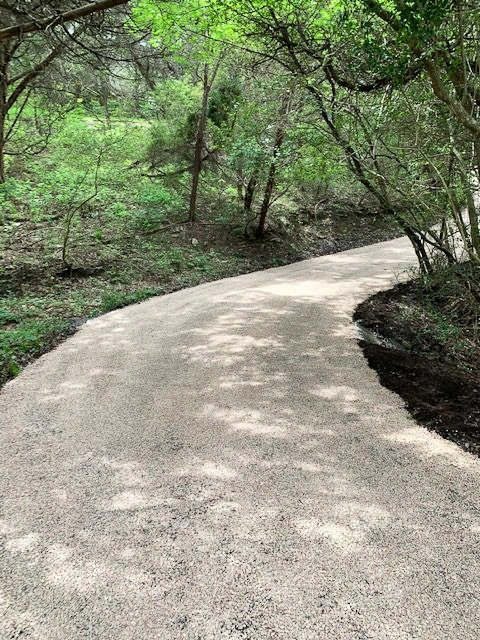 Allée en gravier stabilisé serpentant dans un sous-bois, sans bordure apparente