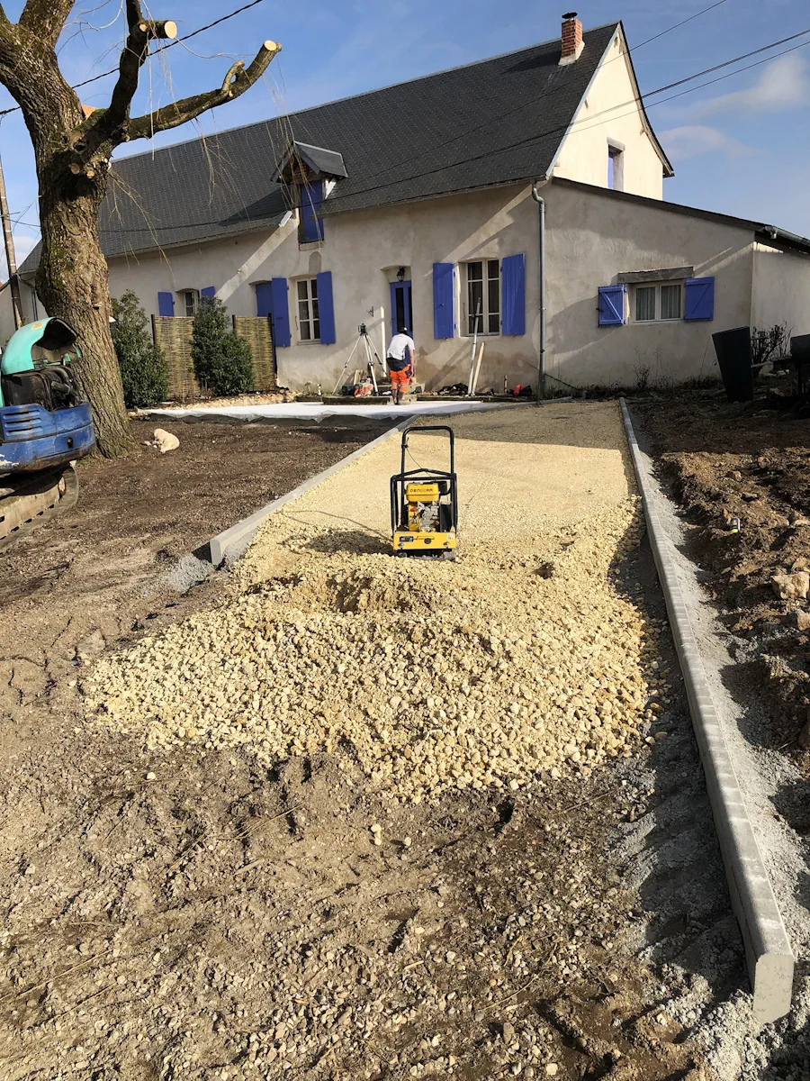 Plaque vibrante compactant le gravier d'une cour, mini-pelle en attente