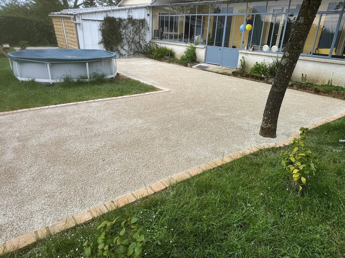 Cour en gravier stabilisé devant une véranda vitrée, bordée de pavés, avec une piscine hors-sol sur la pelouse