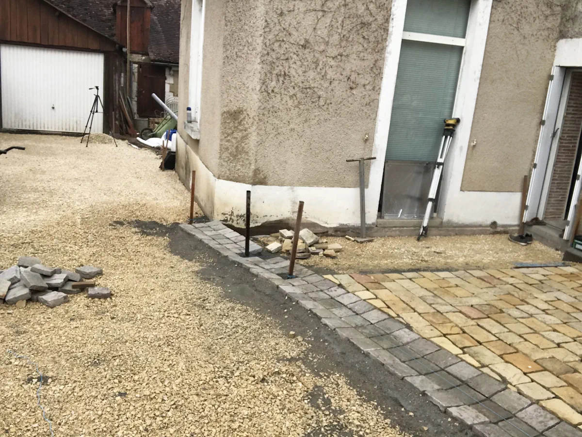 Cour en gravier et pavage rattrapant les seuils d'une maison, piquets de niveau en place