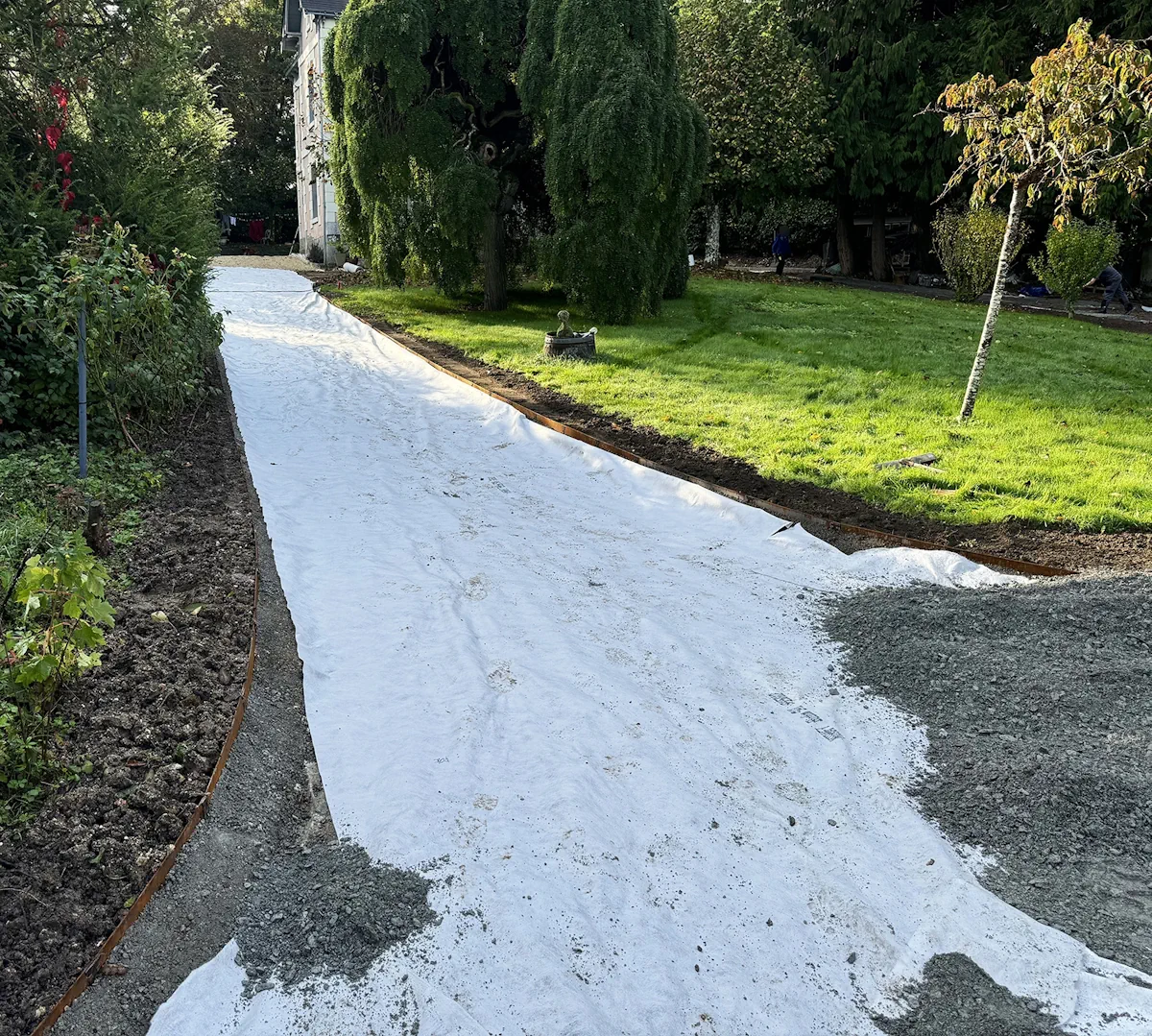 Géotextile déroulé sur le fond de forme d'une allée, bordure en acier corten posée