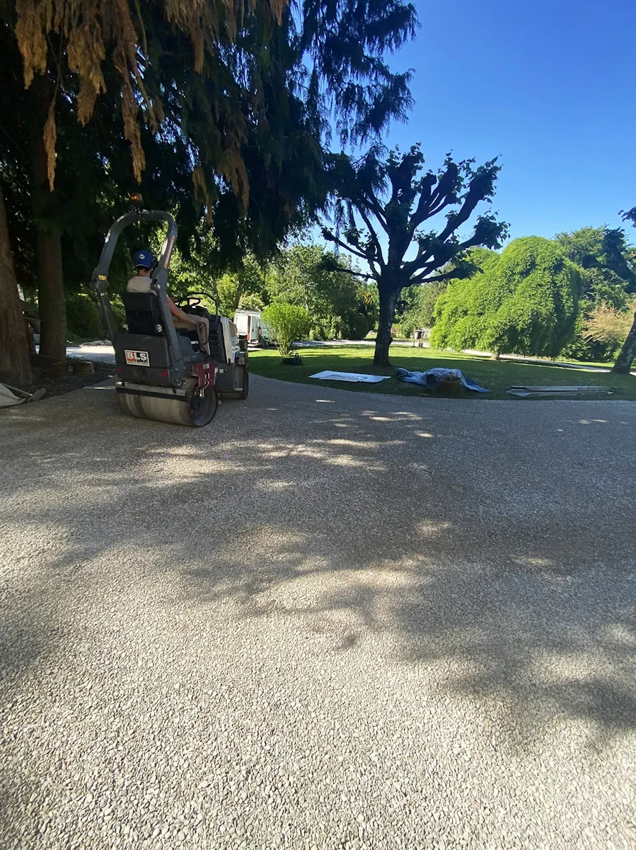 Rouleau compresseur sur une vaste cour en gravier, dans un parc arboré