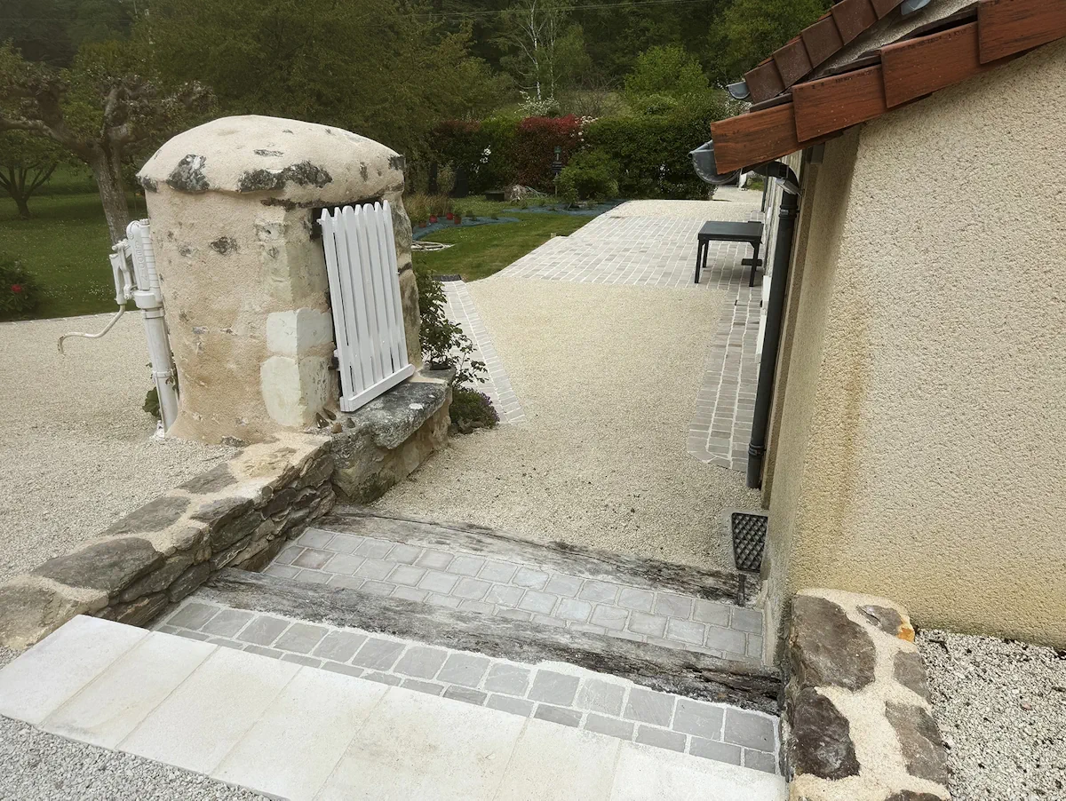 Emmarchement en pavés de pierre reliant une cour en gravier à une terrasse, le long d'une maison ancienne