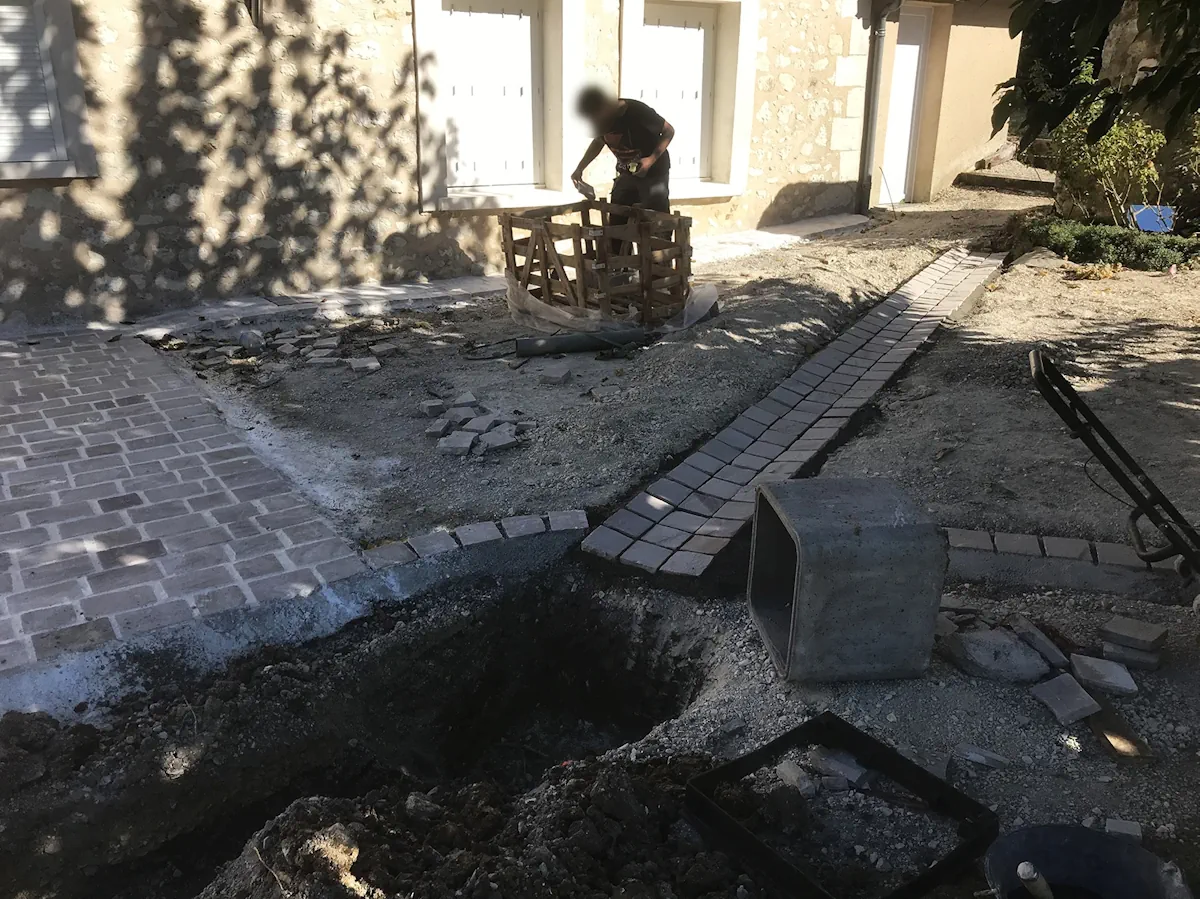 Cour en cours de pavage avec un regard béton en attente de raccordement