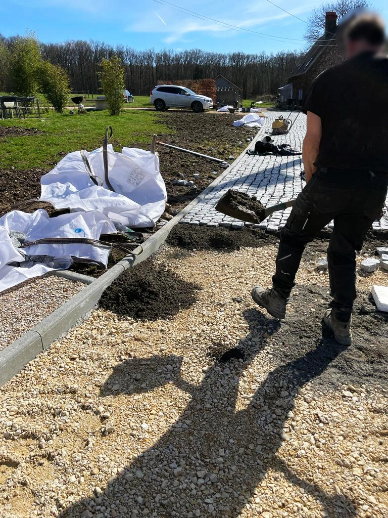 Compagnon travaillant à la pose de pavés le long d'une bordure béton, big-bags de matériaux à proximité