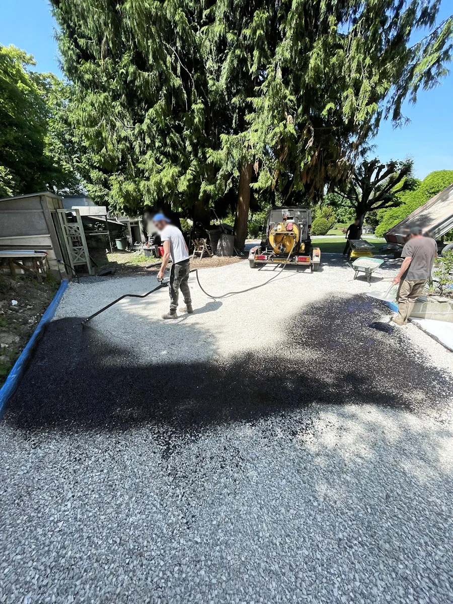 Deux compagnons appliquant un liant sur une cour en gravier, machine sur remorque à l'arrière