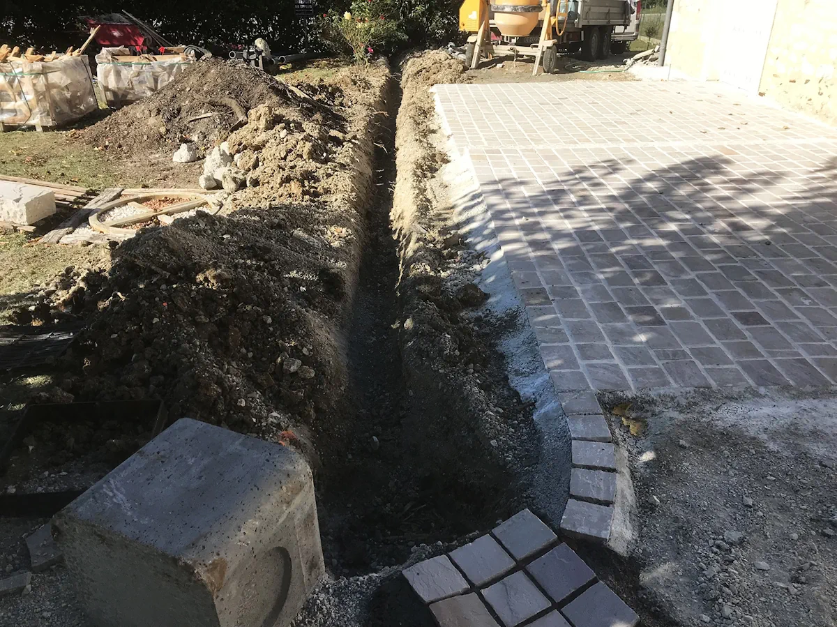 Tranchée ouverte le long d'une cour pavée neuve, toupie à béton à l'arrière