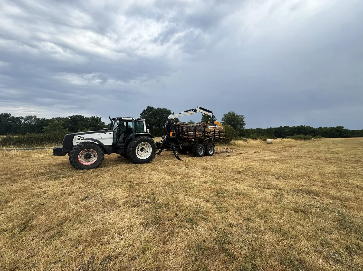 Tracteur et remorque forestière à grue chargés de bois, au milieu d'un champ moissonné