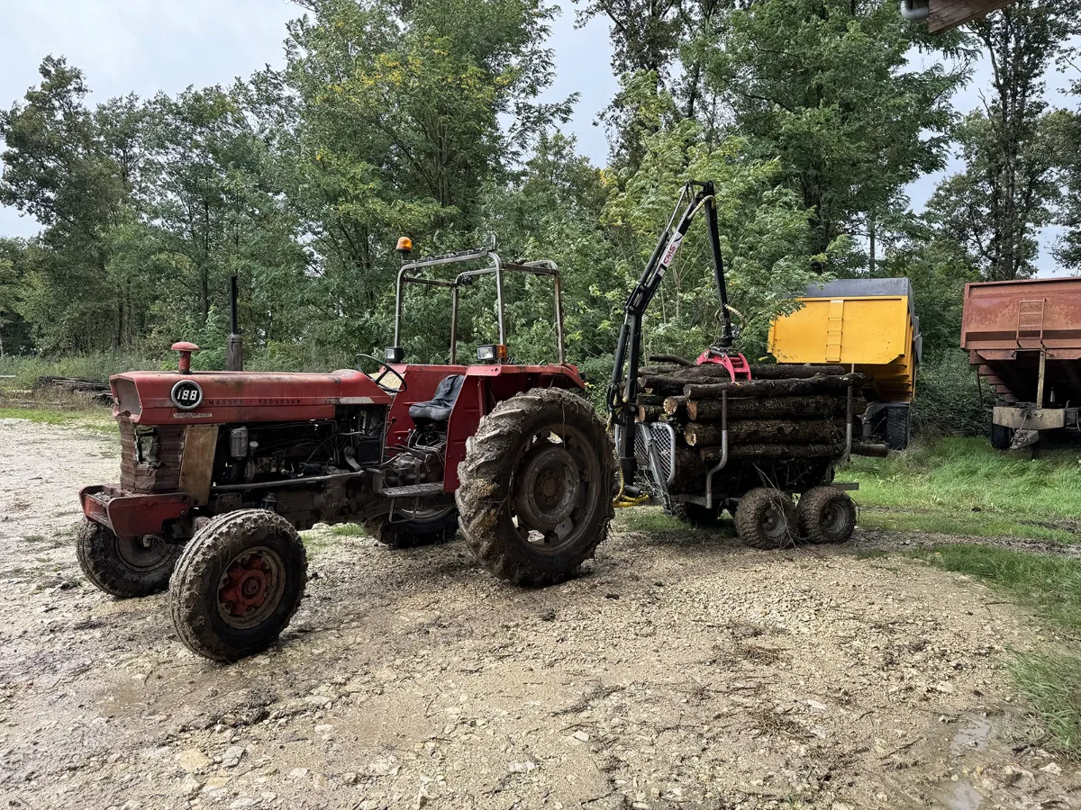 Tracteur agricole rouge attelé à une remorque forestière à grue, sur une aire de dépôt