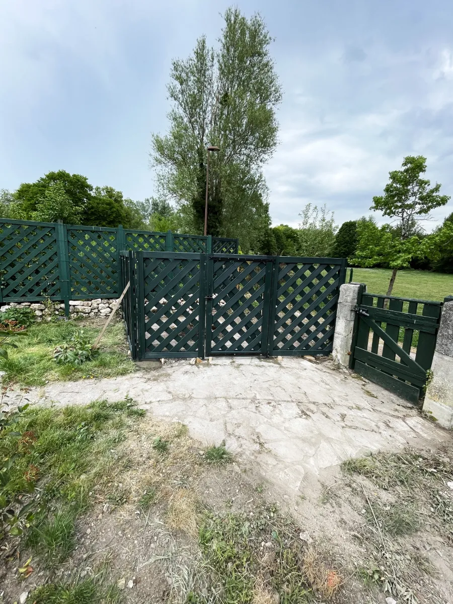 Panneaux de treillis en bois peint vert foncé avec portillon, sur une cour en pierre