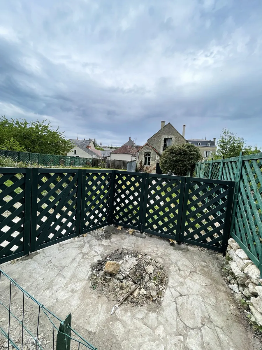 Panneaux de treillis en bois vert foncé fermant une terrasse en pierre, vue sur les toits