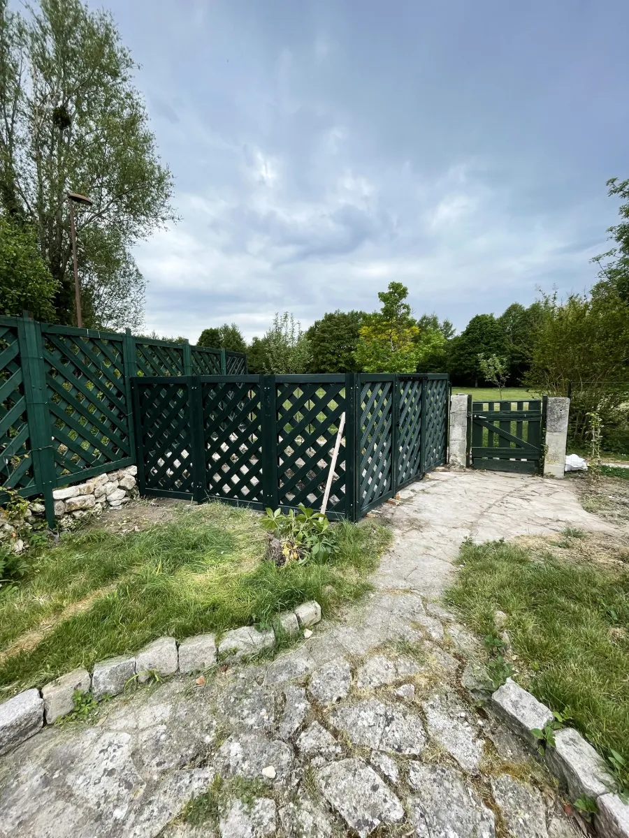 Clôture en treillis de bois vert avec portillon, fermant l'accès d'une cour pavée