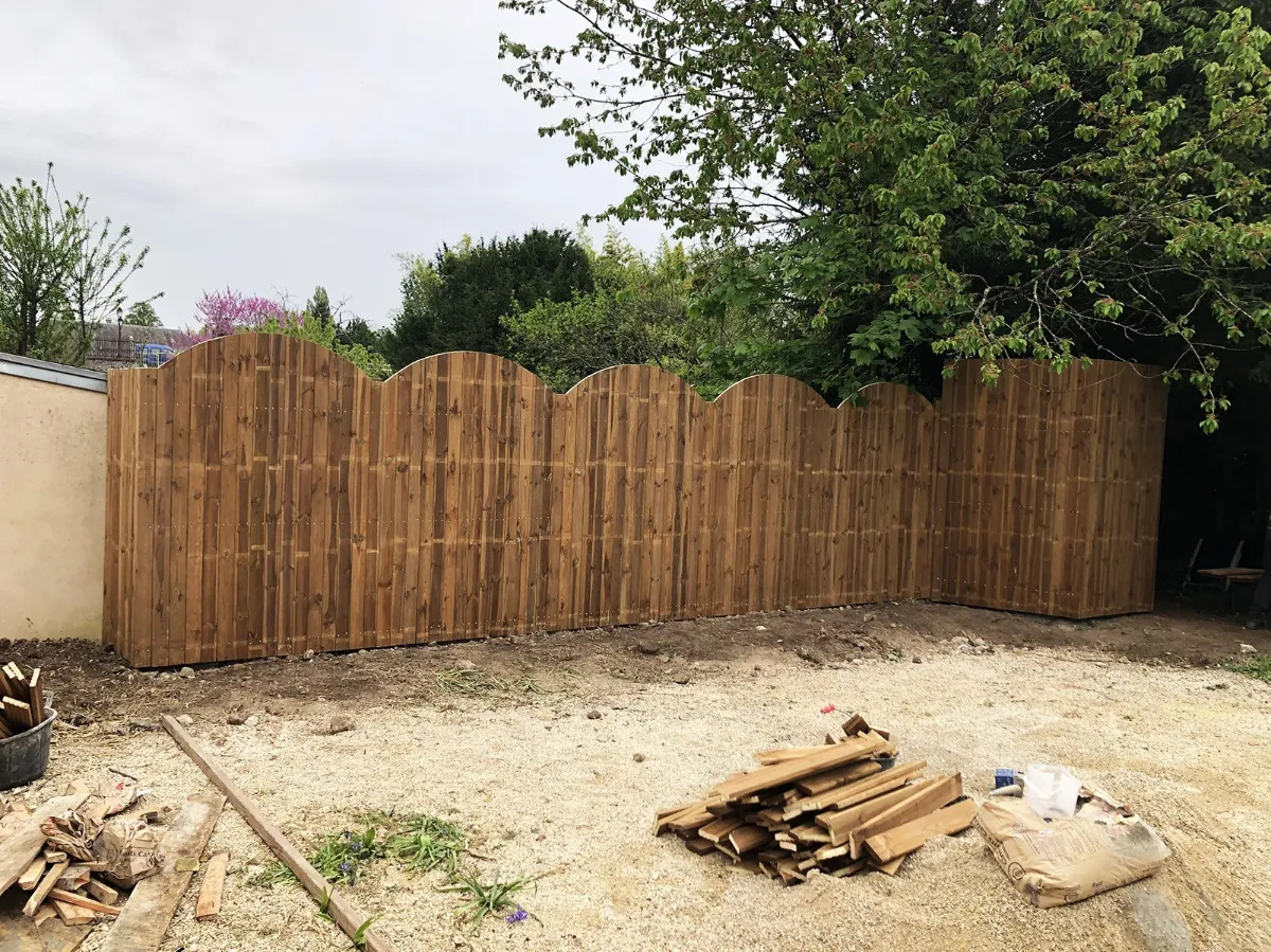 Palissade en bois à l'arase arrondie fermant un jardin, chantier en cours de finition