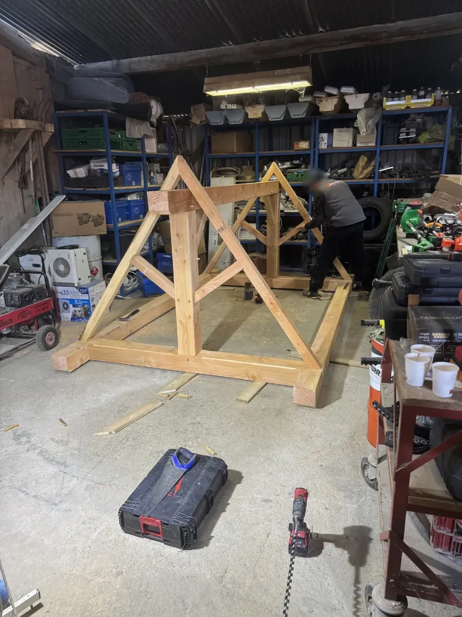 Compagnon assemblant les fermes de charpente en bois dans l'atelier, visseuse et outillage au sol