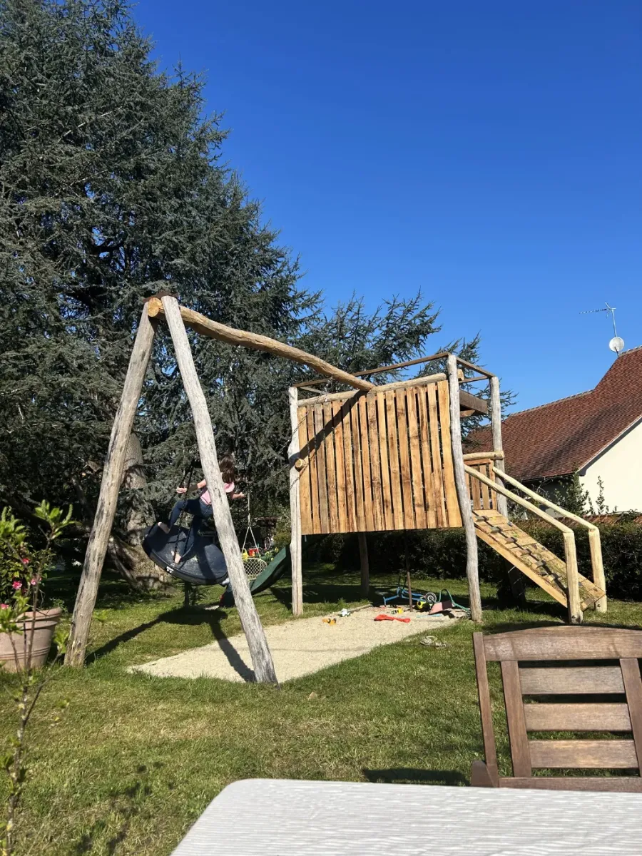 Aire de jeux en bois terminée, avec cabane sur pilotis, balançoire nid et bac à sable