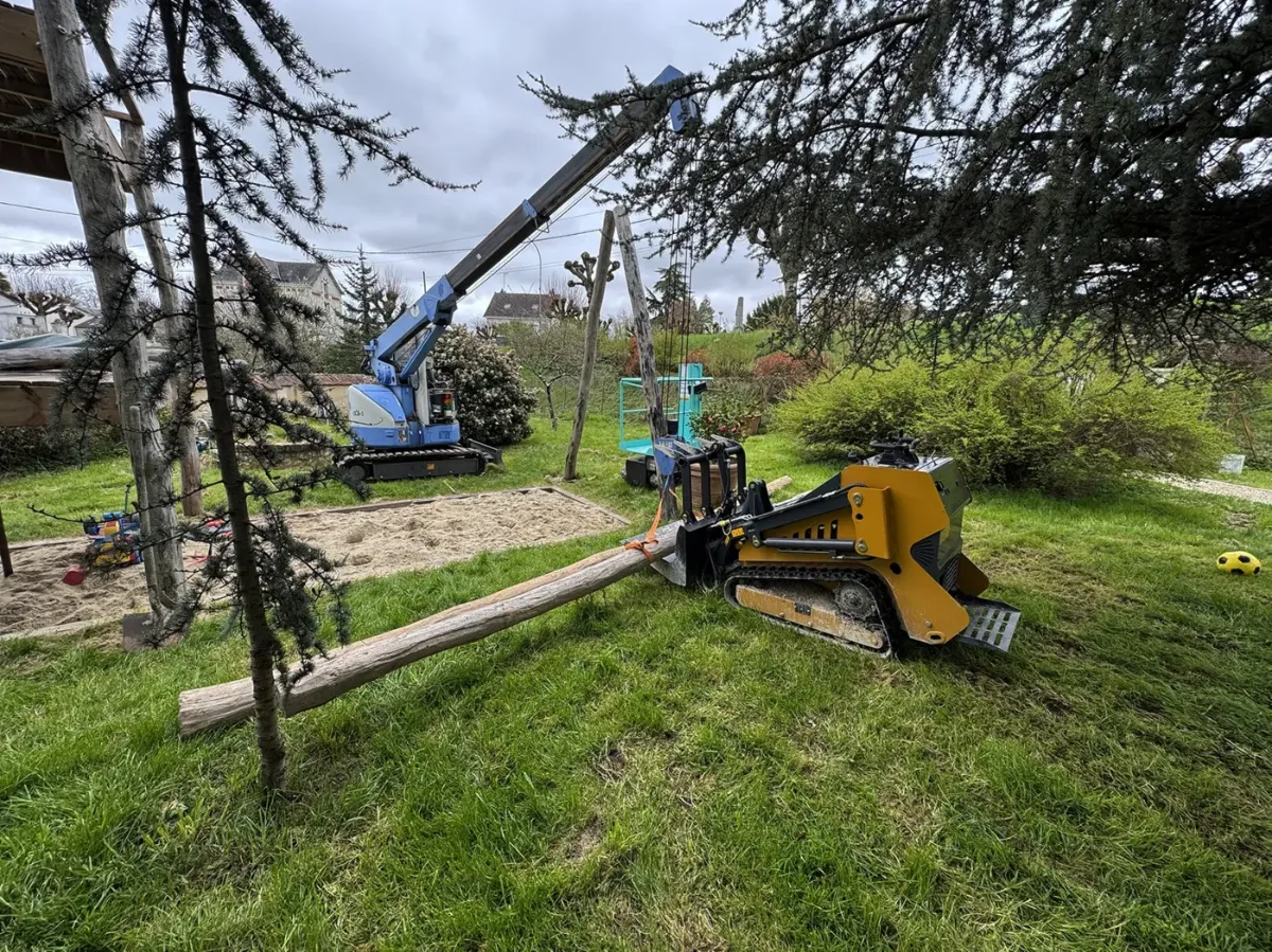 Grue araignée et chargeuse compacte transportant un poteau de bois sur le chantier d'une aire de jeux