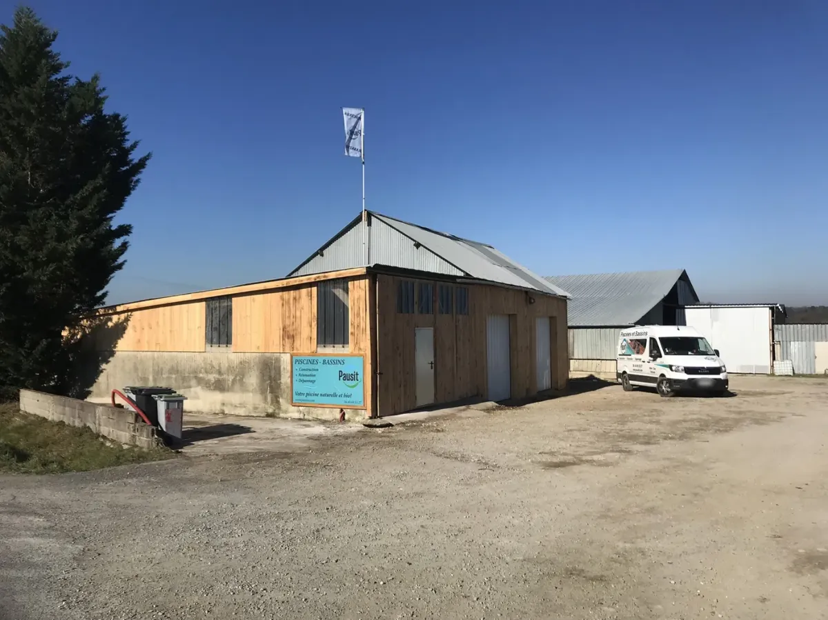 Hangar entièrement habillé d'un bardage en lames de douglas, sous un ciel bleu, fourgon Pausity garé