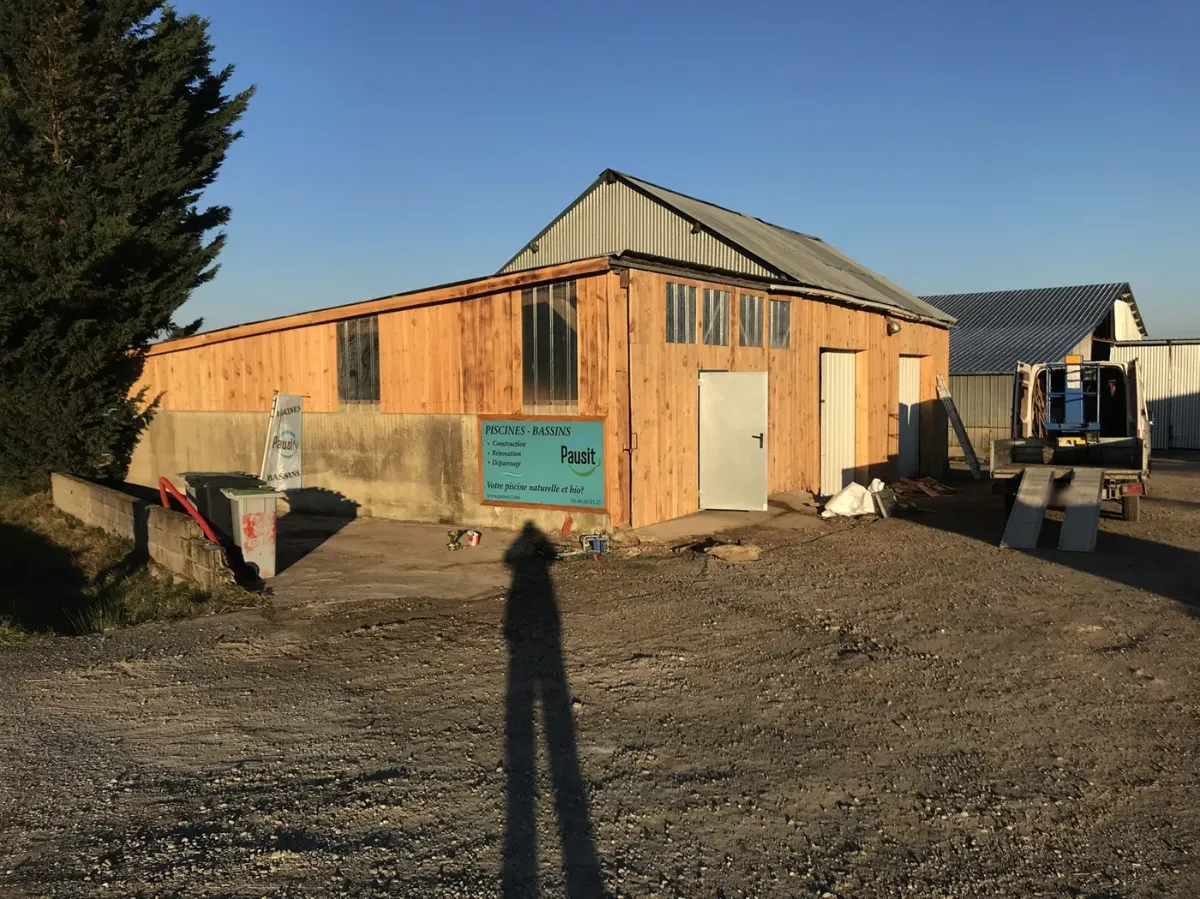 Hangar au bardage bois neuf éclairé par le soleil couchant, panneau Pausity en façade