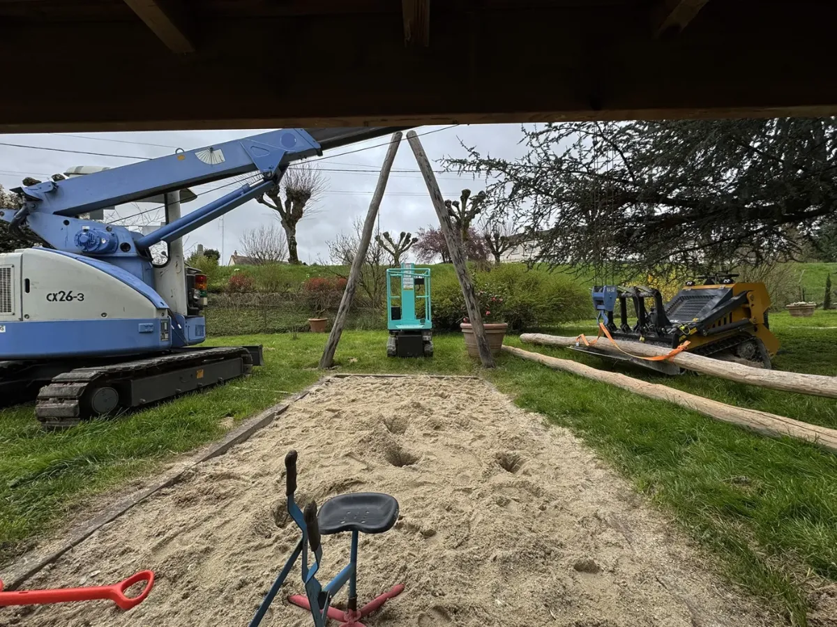 Grue araignée levant la poutre maîtresse d'une aire de jeux en bois, nacelle et chargeuse sur le chantier