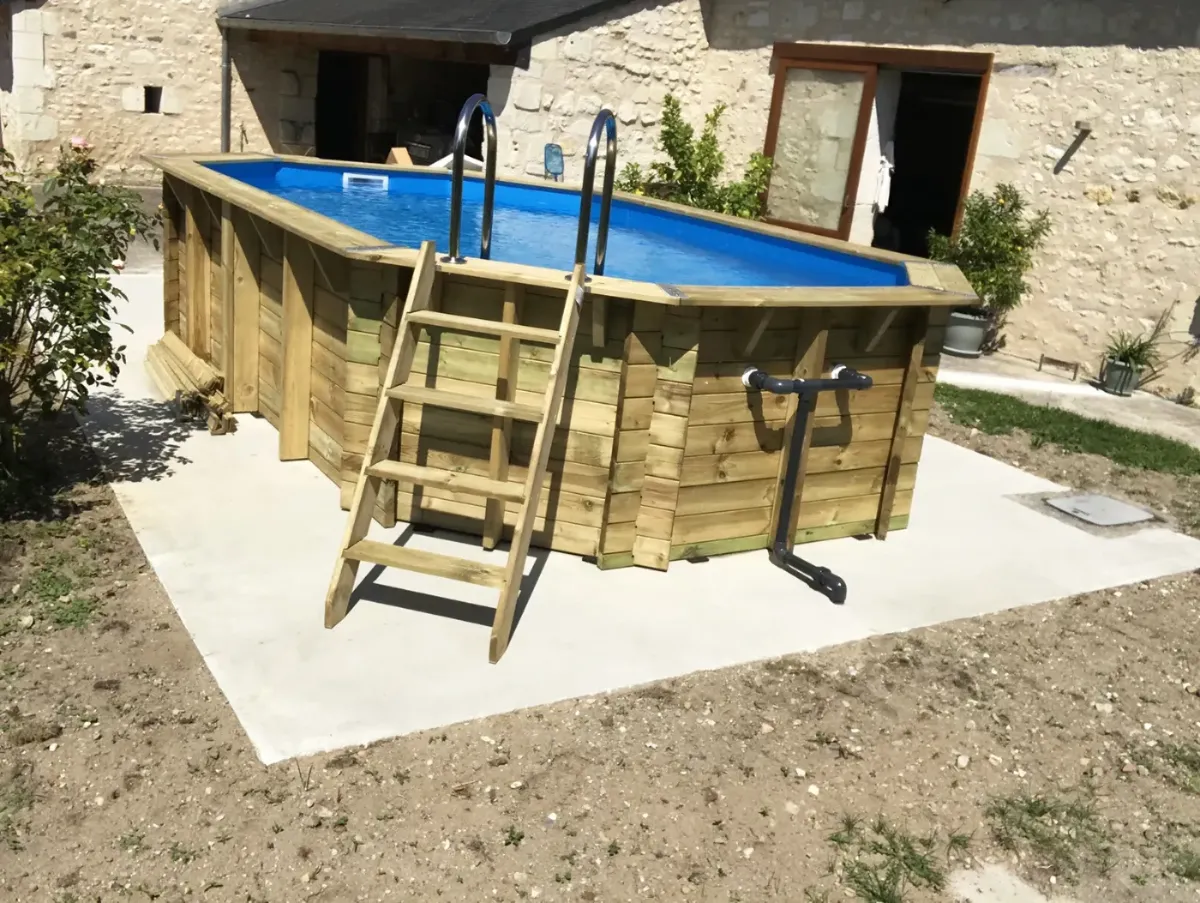 Piscine hors-sol en madriers de bois posée sur dalle béton, dans une cour bordée de murs de tuffeau