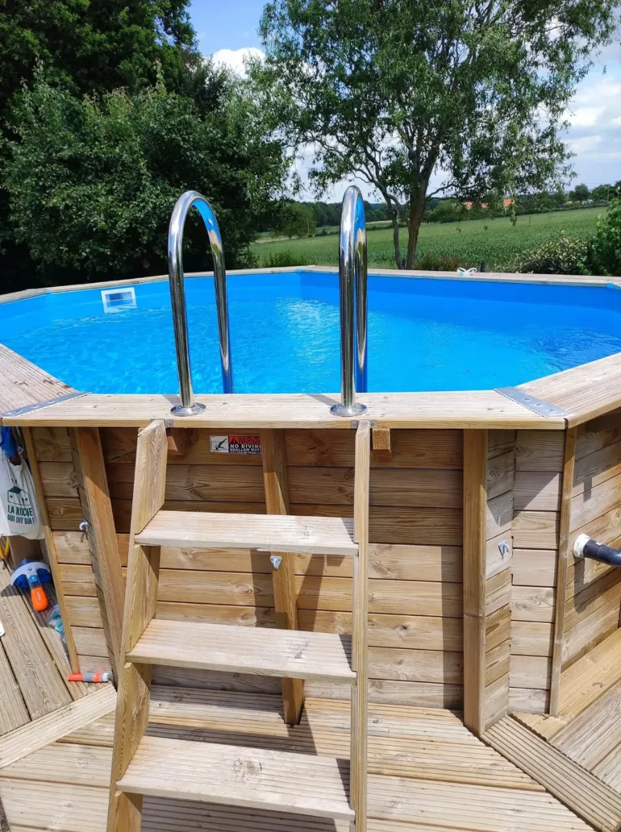 Piscine octogonale en madriers de bois avec échelle, ouverte sur la campagne