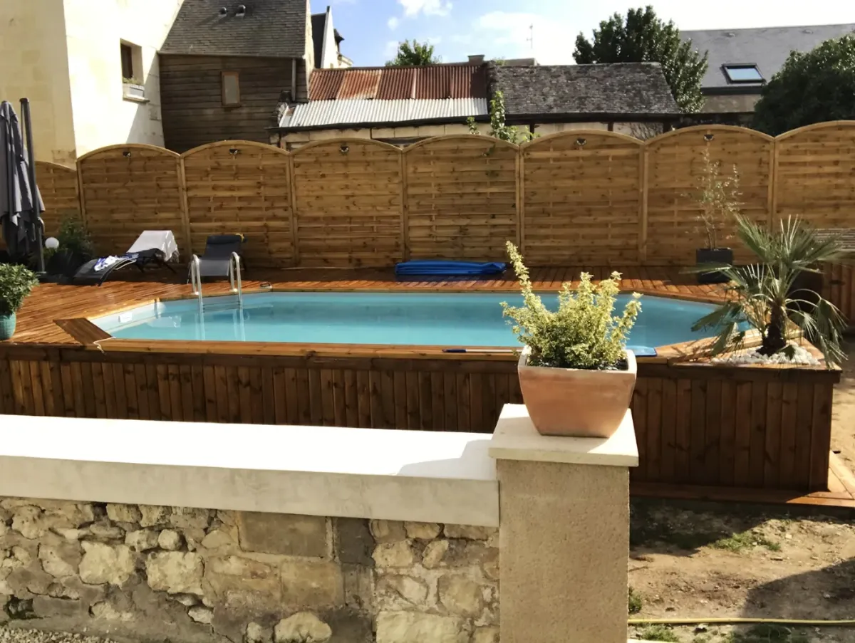 Piscine en bois et sa terrasse dans un jardin de ville, cernées de palissades à l'arase cintrée