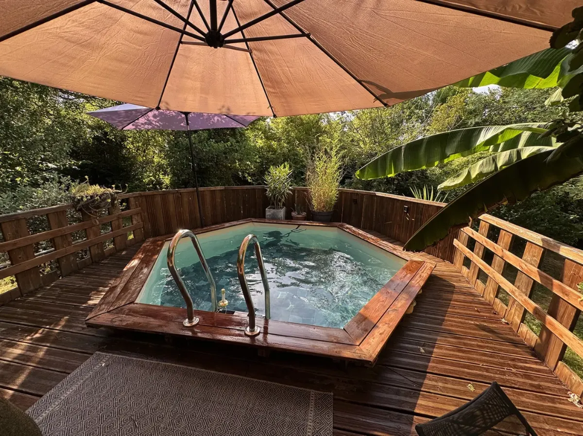 Piscine hexagonale encastrée dans une terrasse en bois, parasols et massifs autour