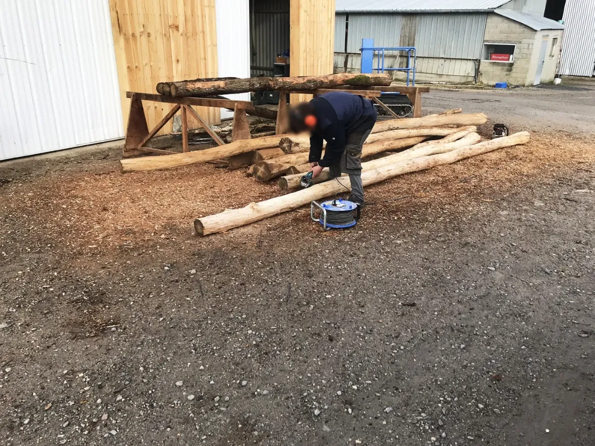 Compagnon ponçant un poteau de bois écorcé au dépôt, avant montage de l'aire de jeux