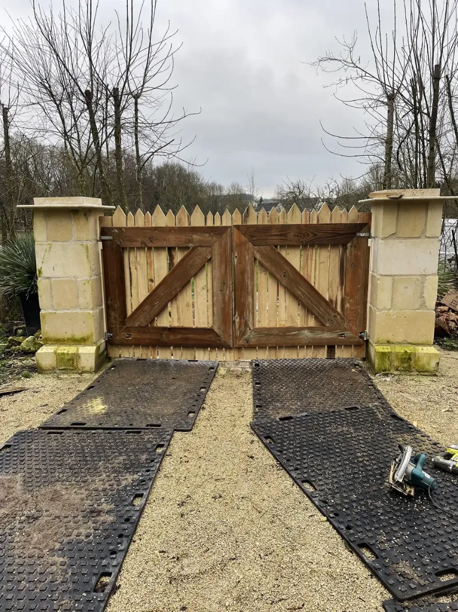 Portail de jardin en bois à claire-voie, à lames pointues et cadre contreventé, entre deux piliers de pierre