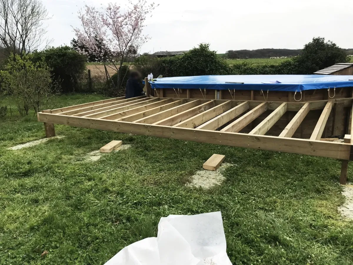Solives de terrasse en cours de pose autour d'une piscine hors-sol, en bordure de prairie