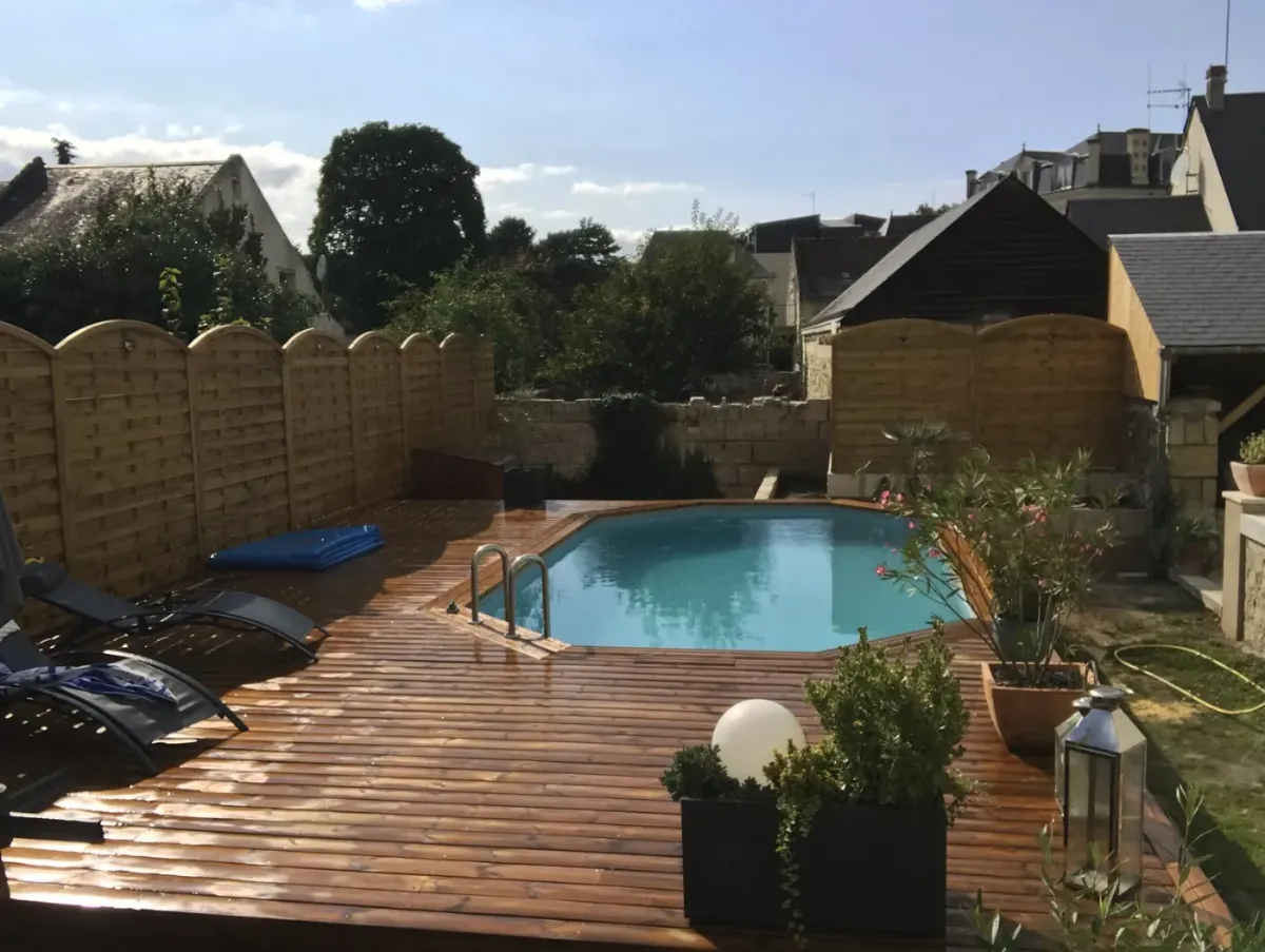 Large terrasse en lames de bois entourant une piscine hors-sol, dans un jardin de ville clos de palissades