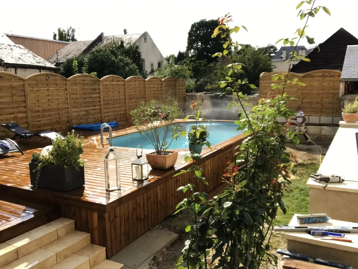 Terrasse en bois lasuré autour d'une piscine, fermée par des panneaux de palissade à l'arase cintrée