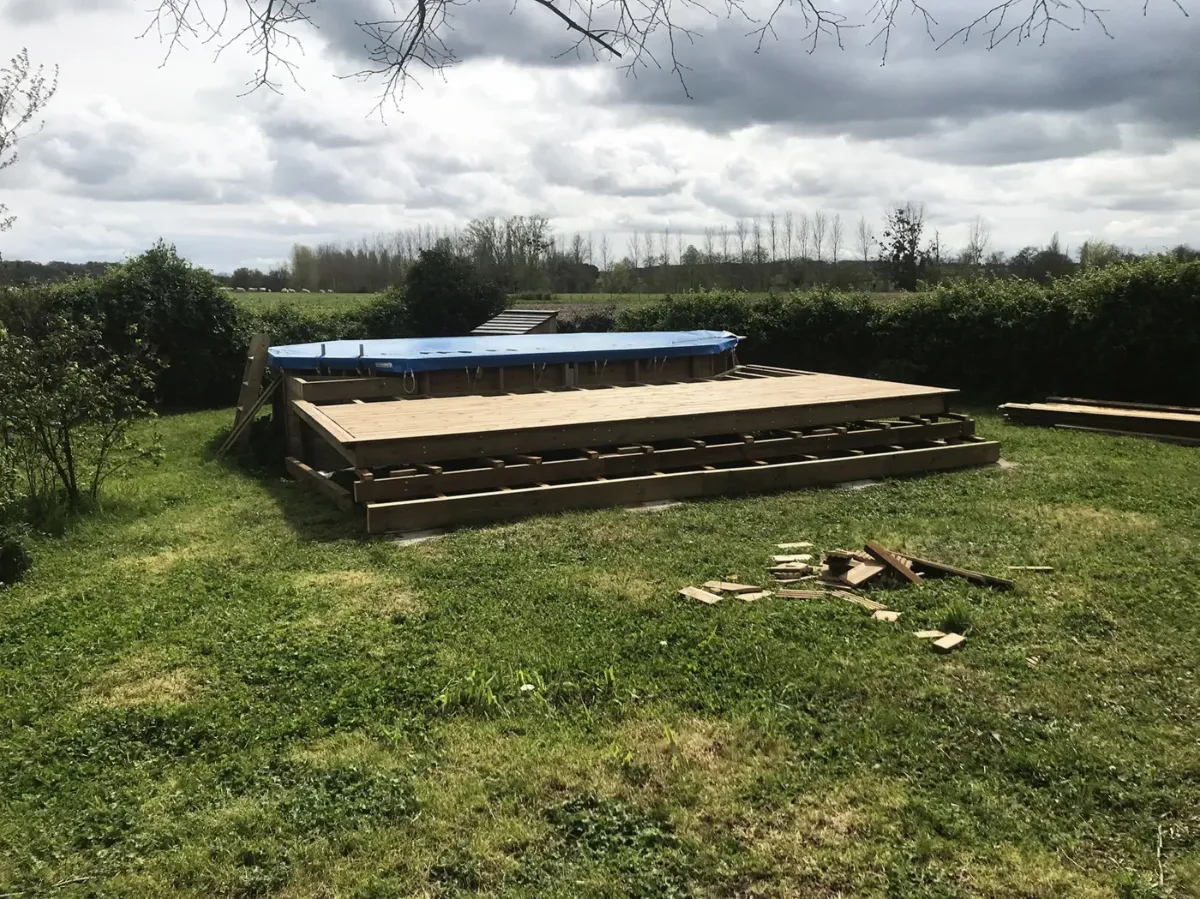 Premières lames de platelage posées sur la structure d'une terrasse de piscine, chutes de bois au sol