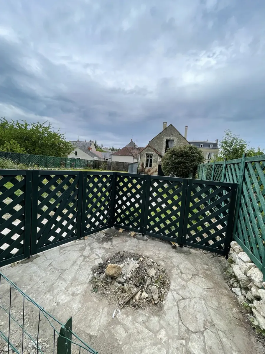 Panneaux de treillis en bois peint vert foncé fermant une terrasse en pierre, vue sur les toits