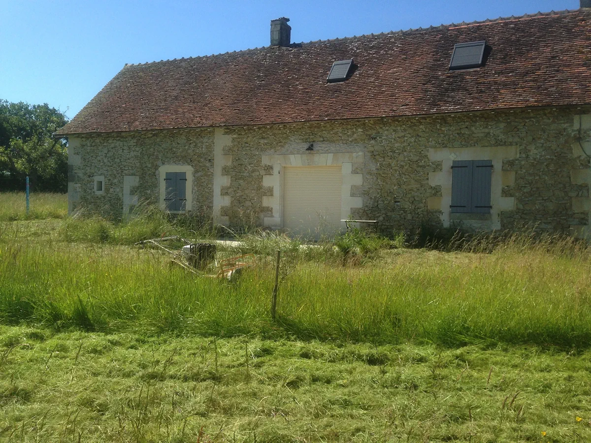 Façade d'une longère de pierre dont la bande d'herbe haute vient d'être ouverte