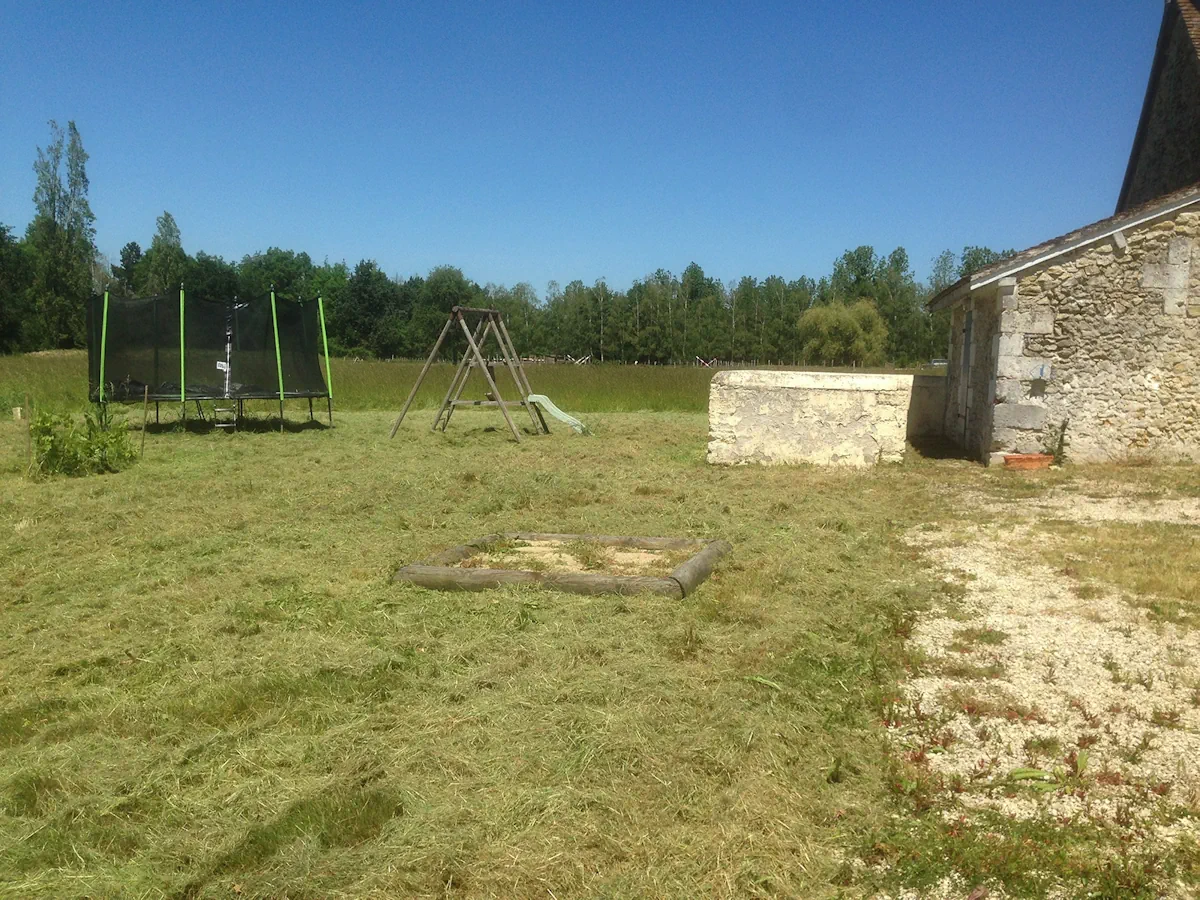Jardin fauché autour d'un portique et d'un trampoline, devant une dépendance de pierre