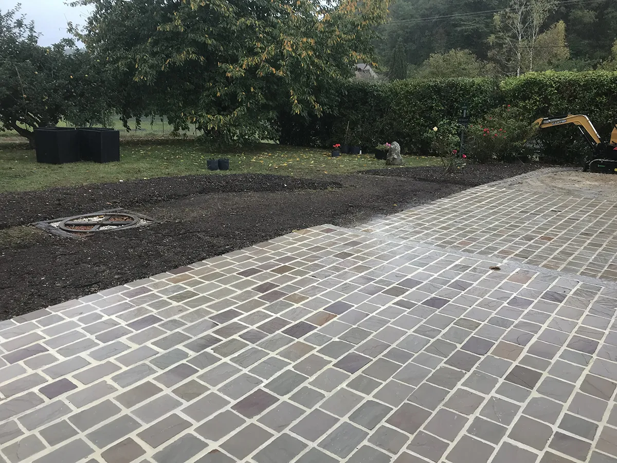 Bande de terre préparée le long d'un pavage de pierre neuf, sous la pluie