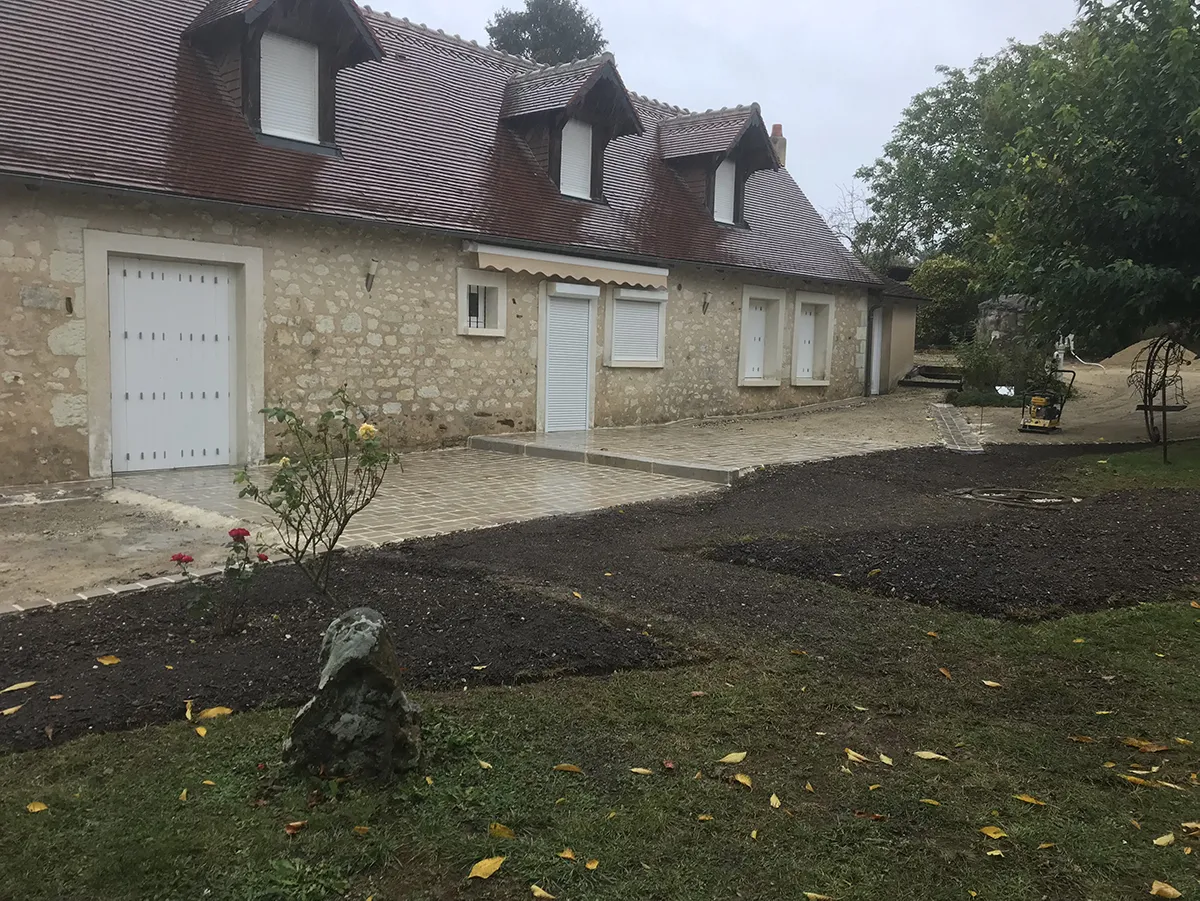 Bandes de terre préparées devant une longère de pierre, sous un ciel d'automne