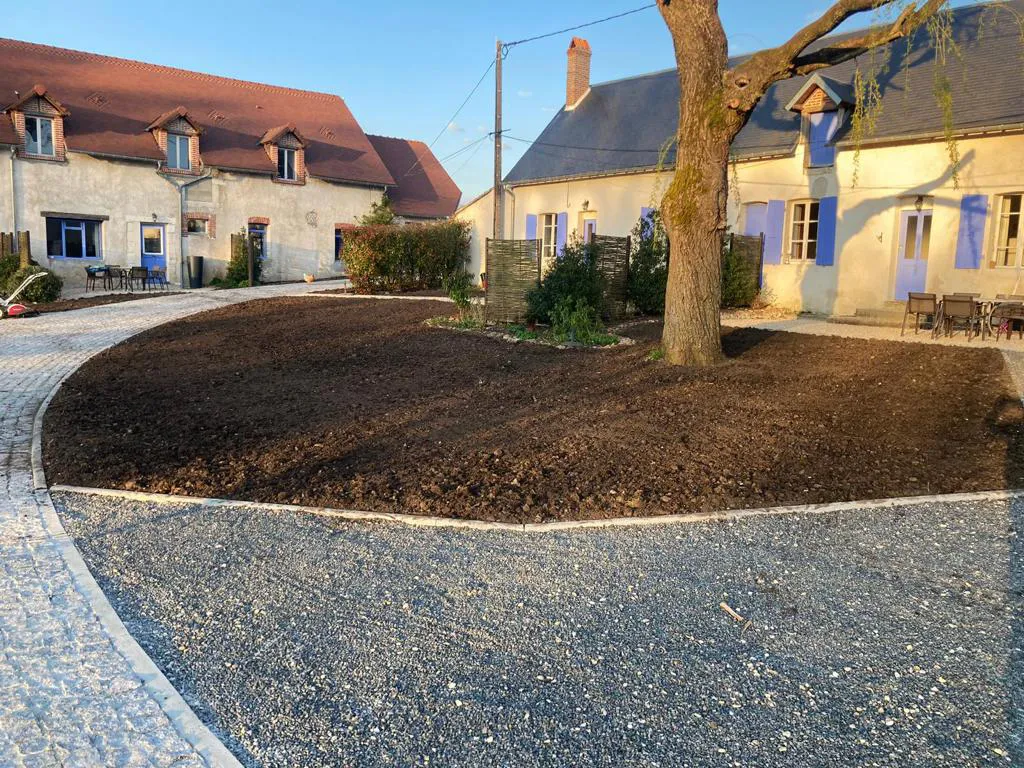 Grande cour de terre préparée entre deux longères, bordée de gravier, avant engazonnement