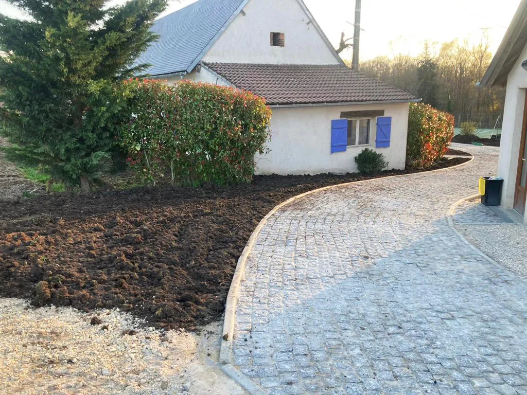 Bande de terre préparée au pied d'une haie de photinias, le long d'une allée pavée