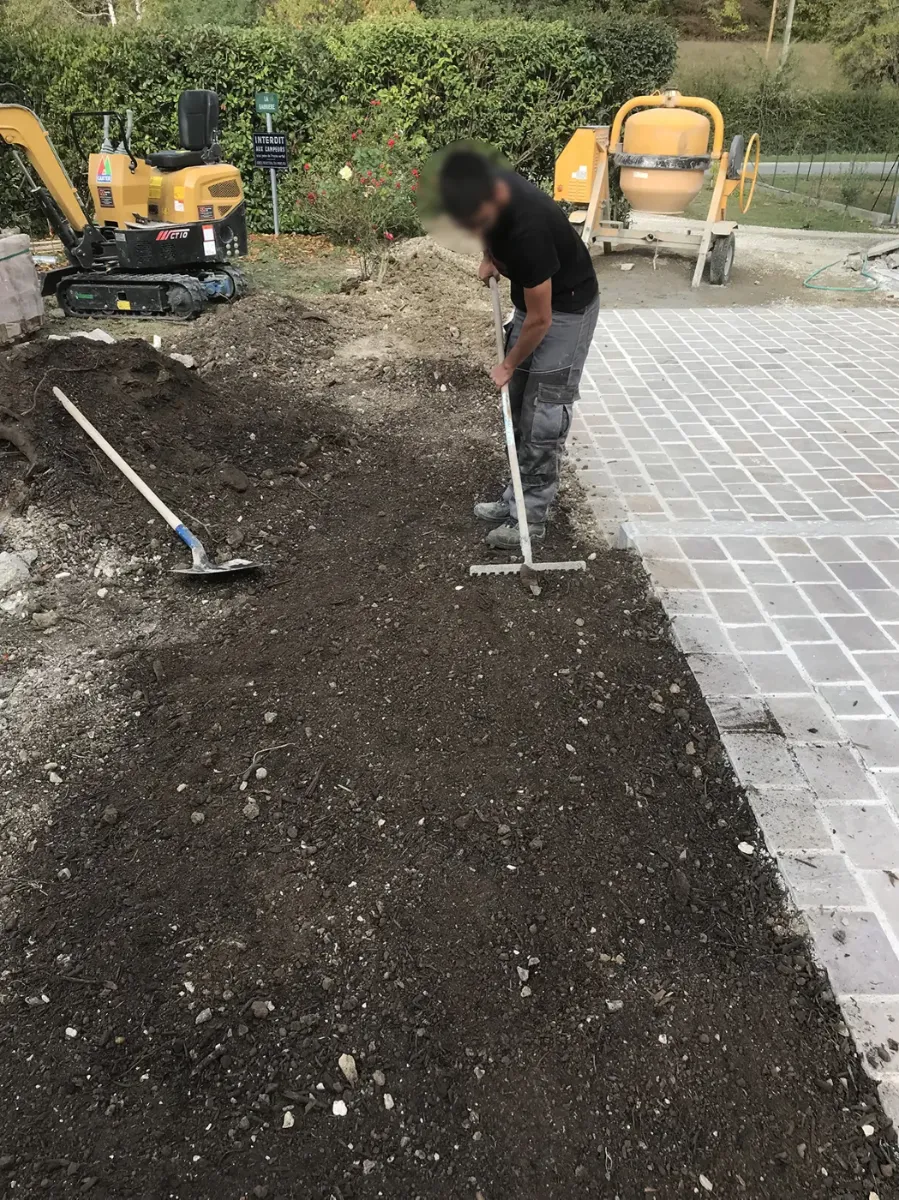 Compagnon nivelant au râteau une bande de terre le long d'une terrasse pavée neuve