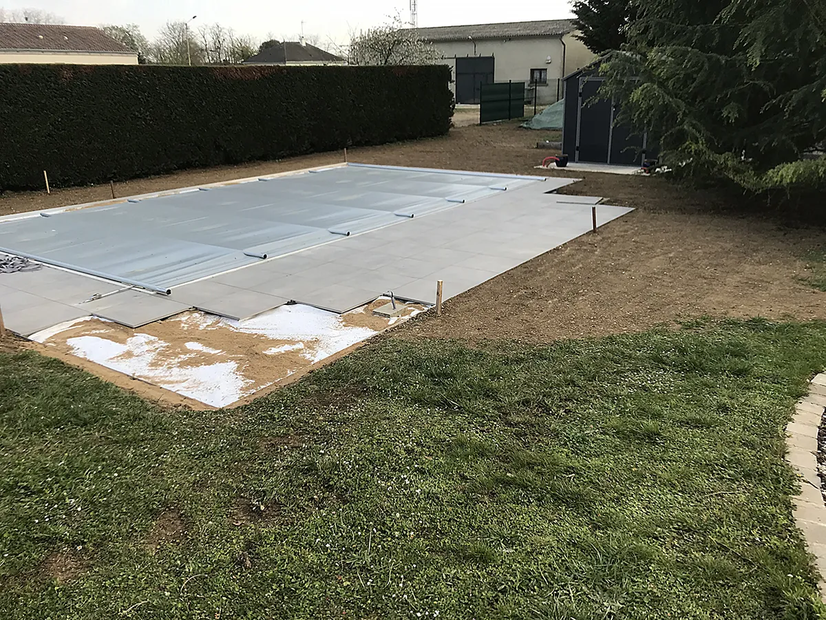 Terrain nu et compacté autour d'une piscine couverte, en limite de pelouse existante