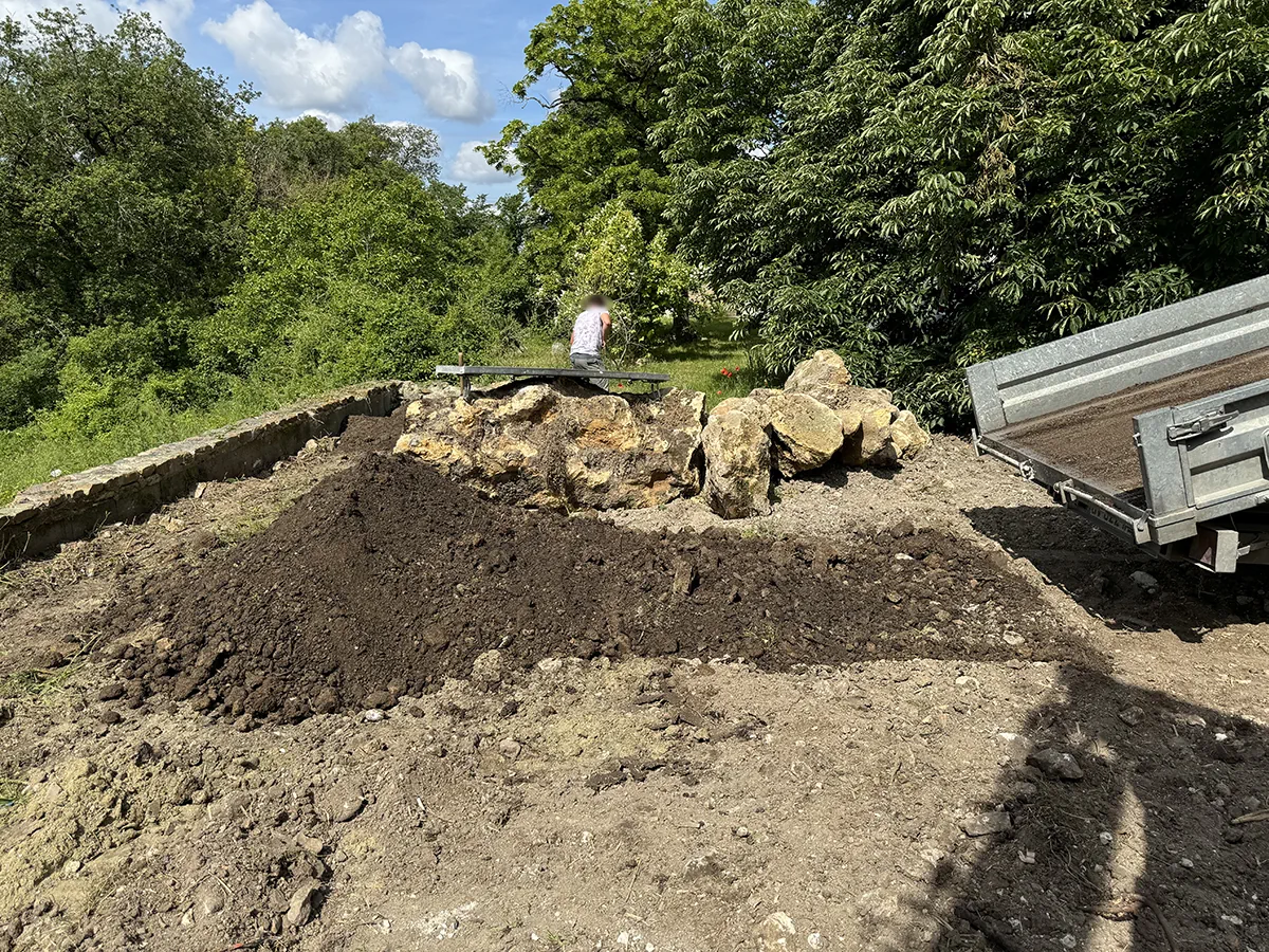 Terre végétale déversée derrière un enrochement neuf, remorque de chantier sur la droite