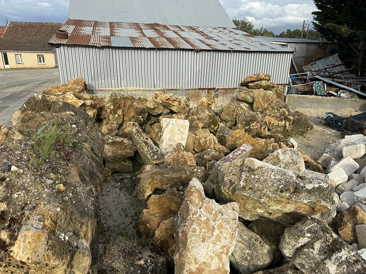 Amoncellement de blocs calcaires et de pierres de récupération devant un hangar de tôle
