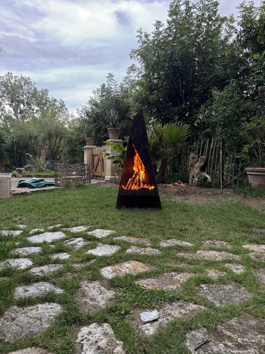 Brasero d'acier en forme de pyramide, feu allumé sous la pluie, sur une aire dallée de pierre